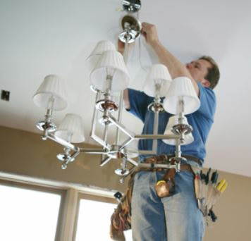 picture of an electrician installing a chandelier to the ceiling of a dining room in Fort Lauderdale, FL