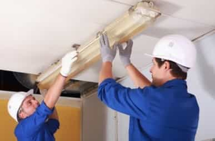 two men lifting and adjusting a lighting fixture on a ceiling